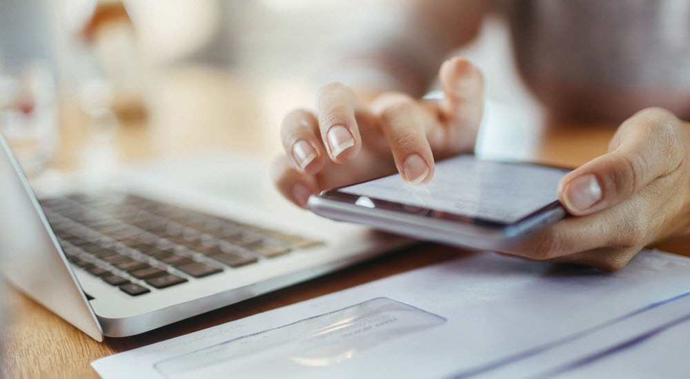 Hand scrolling smartphone screen with laptop in background